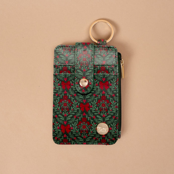 A Merry Moment Keychain Wallet in festive green and red, featuring a gold key ring and a holiday pattern of bows, holly, and sprigs.