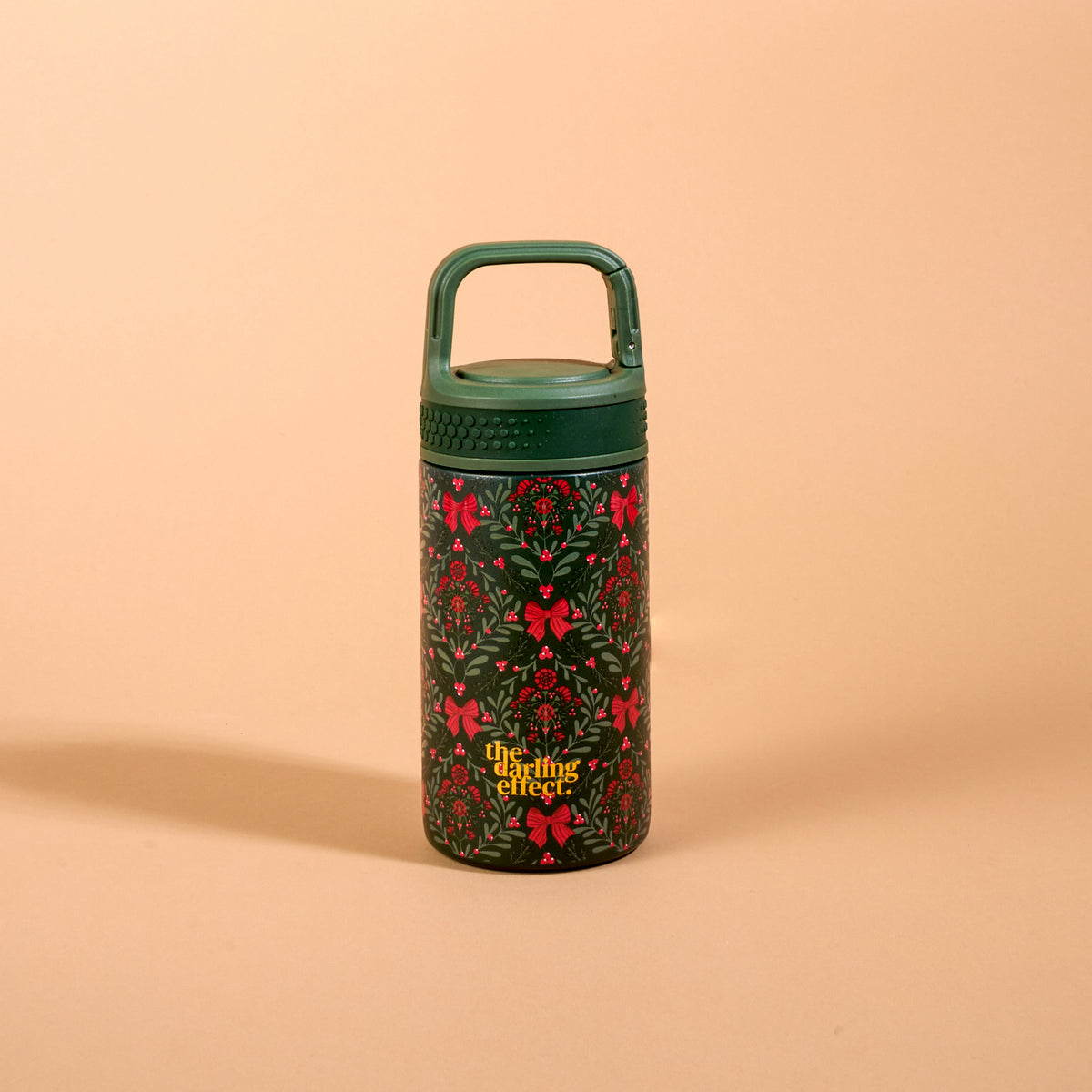 A Merry Moment 6 oz Lil’ Bitty Bottle, a small, 6oz insulated water bottle featuring a festive pattern of red bows, holly, and berries, finished with a green screw-top lid and handle.
