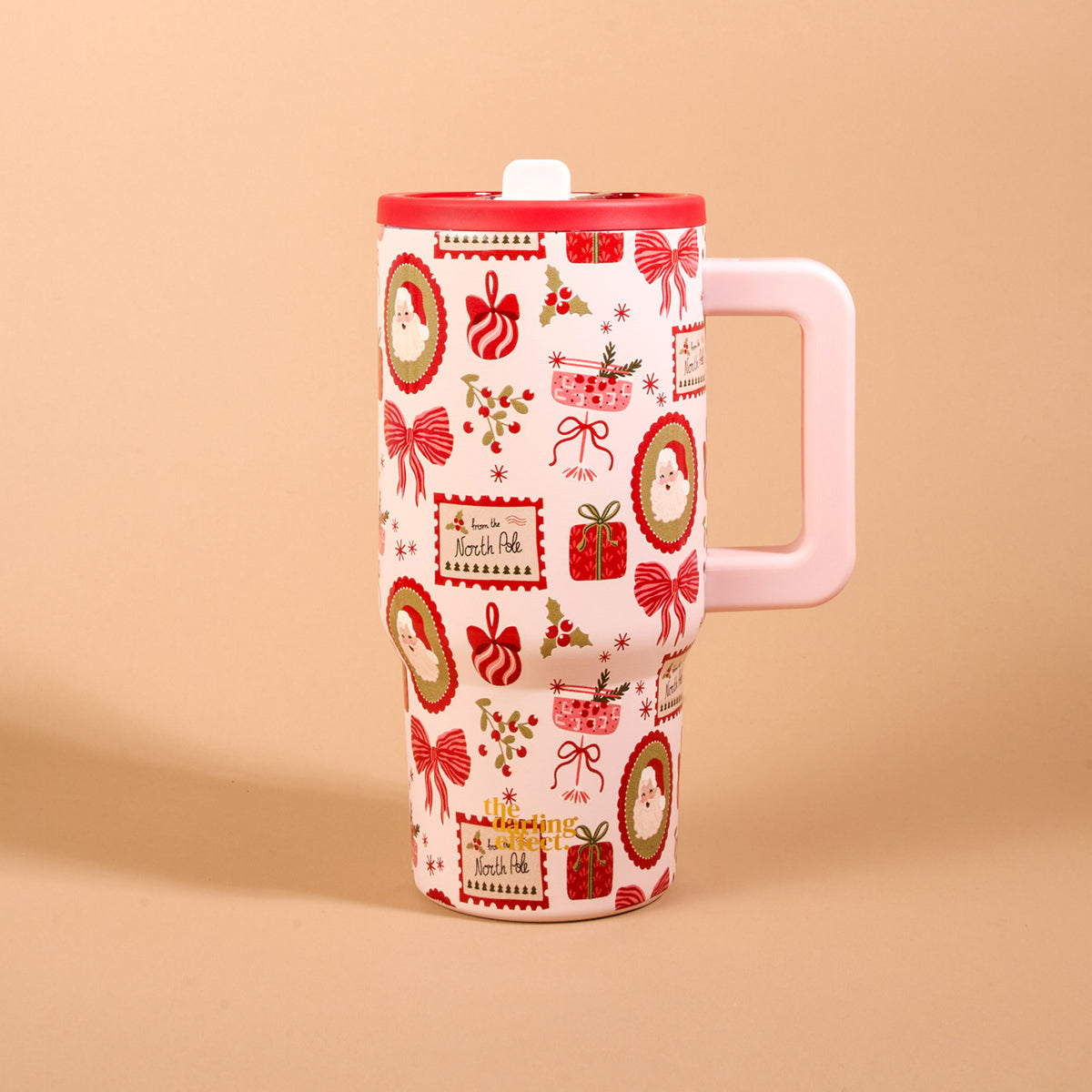 Mistletoe Magic 20 oz Lifestyle Flip Straw Tumbler: 20 oz insulated stainless steel tumbler with a light pink handle, red lid, and a Christmas-themed pattern of Santa portraits, gift boxes, bows, and holly.