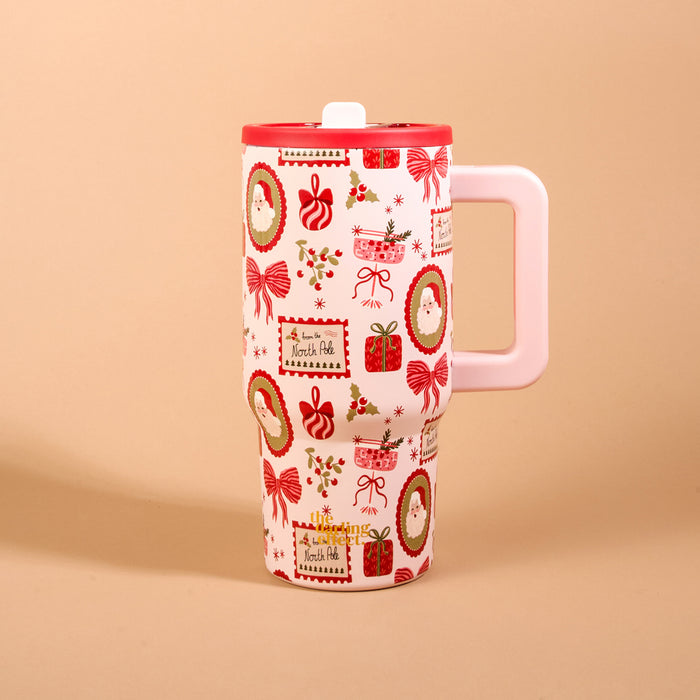 Mistletoe Magic 20 oz Lifestyle Flip Straw Tumbler: 20 oz insulated stainless steel tumbler with a light pink handle, red lid, and a Christmas-themed pattern of Santa portraits, gift boxes, bows, and holly.