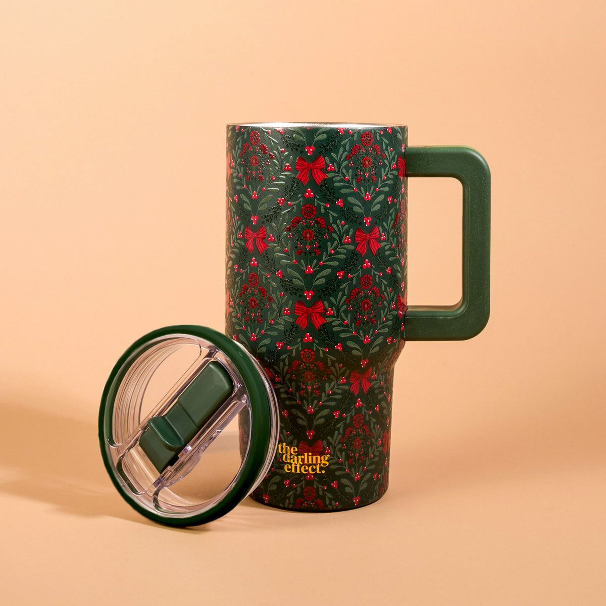 A Merry Moment 20 oz Lifestyle Flip Straw Tumbler in dark green, featuring a holiday pattern of red bows, berries, and evergreen sprigs with a matching side handle.