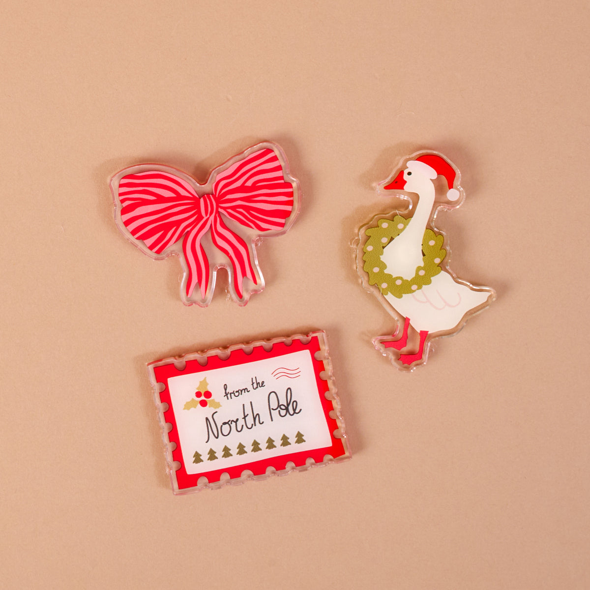 Tis the Season Little Magnet Set featuring three acrylic magnets: a red and pink striped bow, a goose wearing a Santa hat and green wreath, and a rectangular stamp labeled from the North Pole.