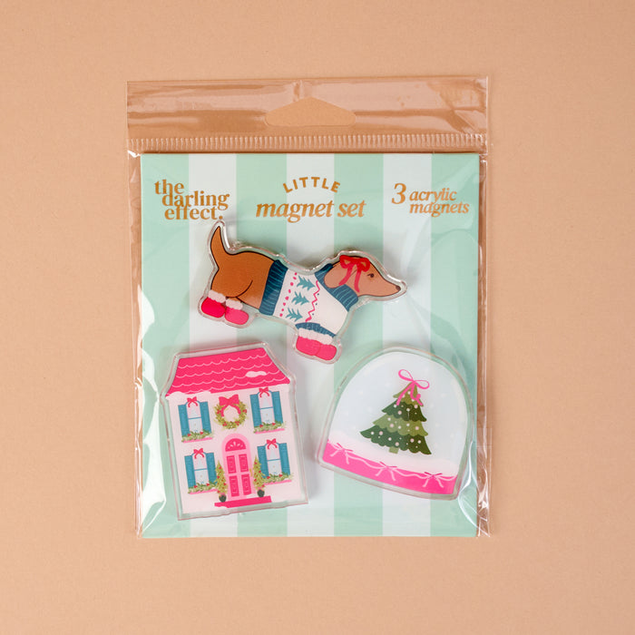 Winter Daydream Little Magnet Set featuring a dachshund in a sweater, a pink house with a wreath, and a Christmas tree inside a snow globe.