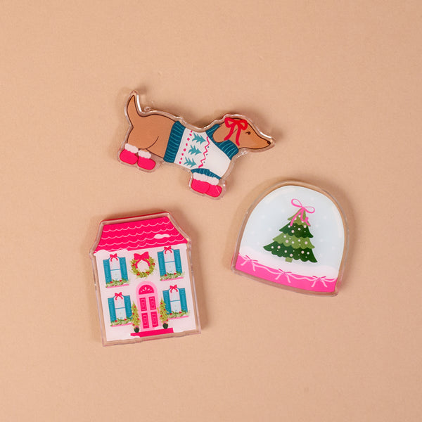Winter Daydream Little Magnet Set featuring three decorative acrylic magnets: a dachshund in a sweater, a snow globe with a Christmas tree, and a two-story house with holiday decorations.