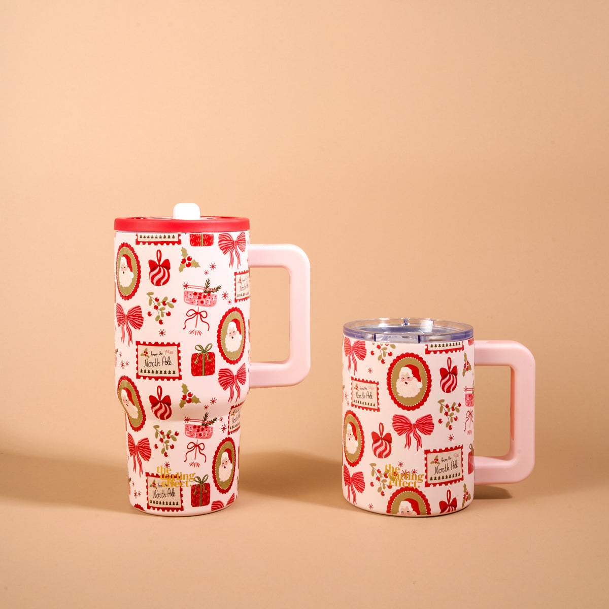 Two Mistletoe Magic 14 oz Insulated Mugs featuring Santa, gifts, and bows, with one tall coffee mug featuring a red lid and one shorter mug with a clear lid.