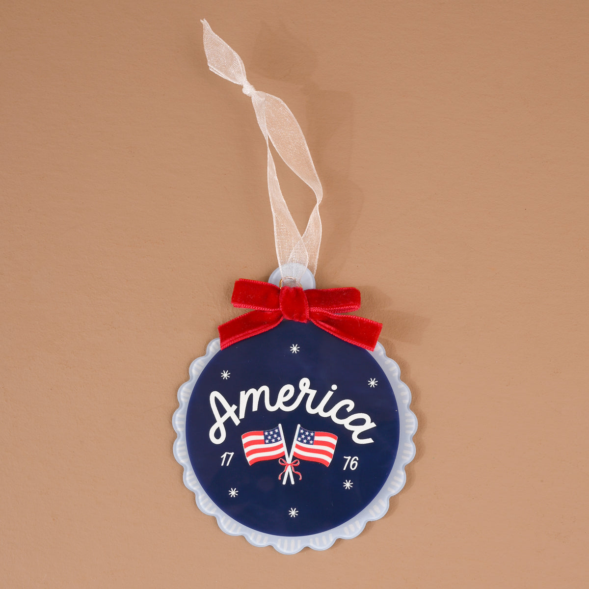 America Acrylic Ornament: A round blue acrylic ornament featuring the word America, two American flags, the years 17 and 76, and a red velvet bow with a white ribbon hanger.