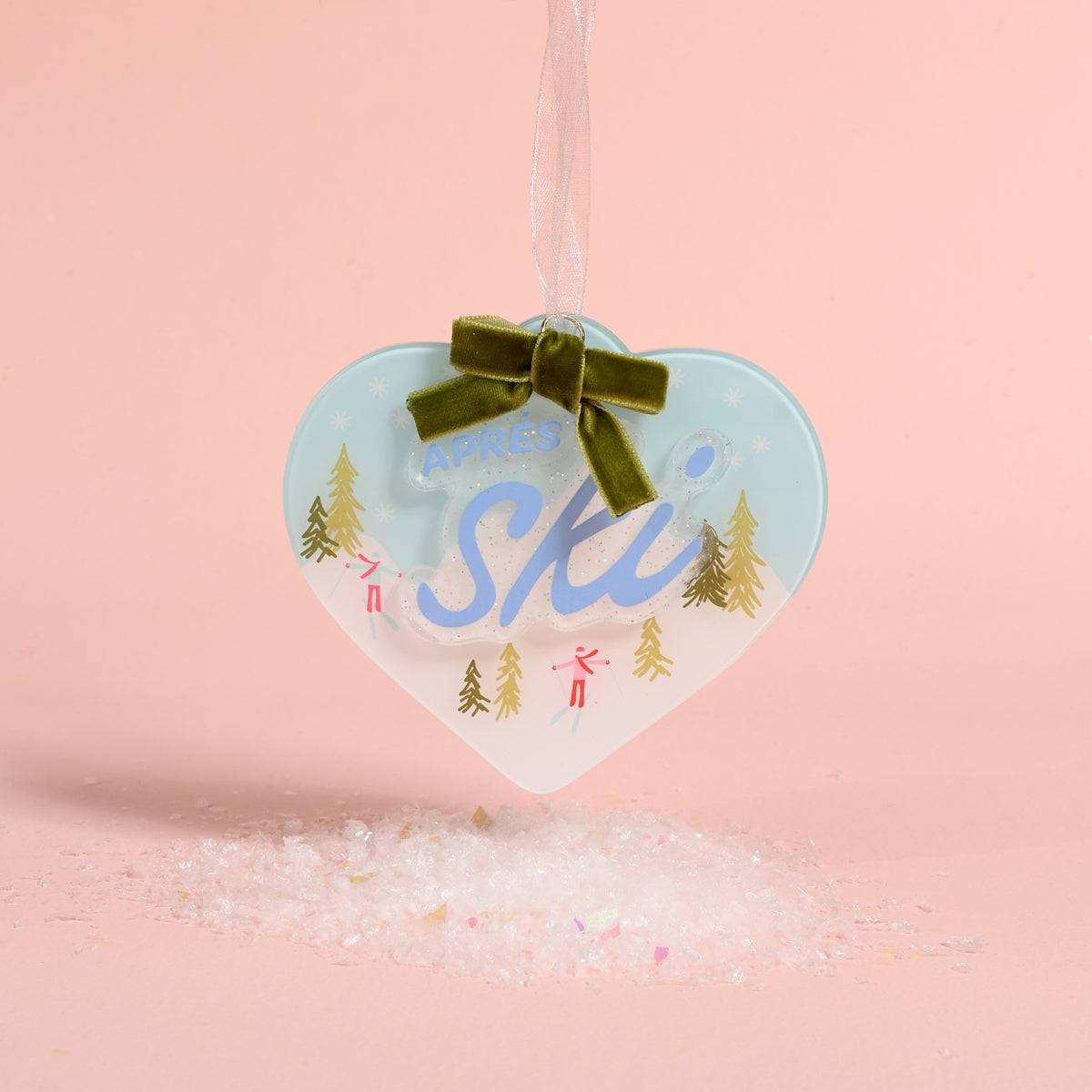 Aprés Ski Acrylic Ornament featuring a heart-shaped design with skiers, pine trees, and a green ribbon topper.