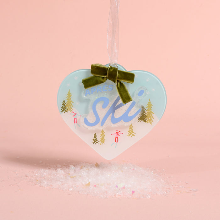Aprés Ski Acrylic Ornament featuring a heart-shaped design with skiers, pine trees, and a green ribbon topper.