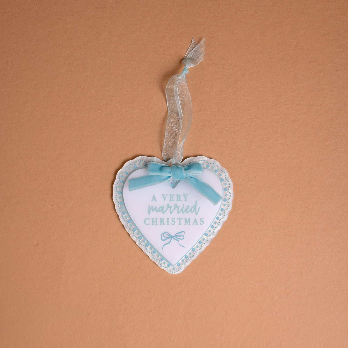 A Very Married Christmas 2026 Acrylic Ornament, featuring a heart-shaped white acrylic design with a blue scalloped border and a light blue ribbon bow.