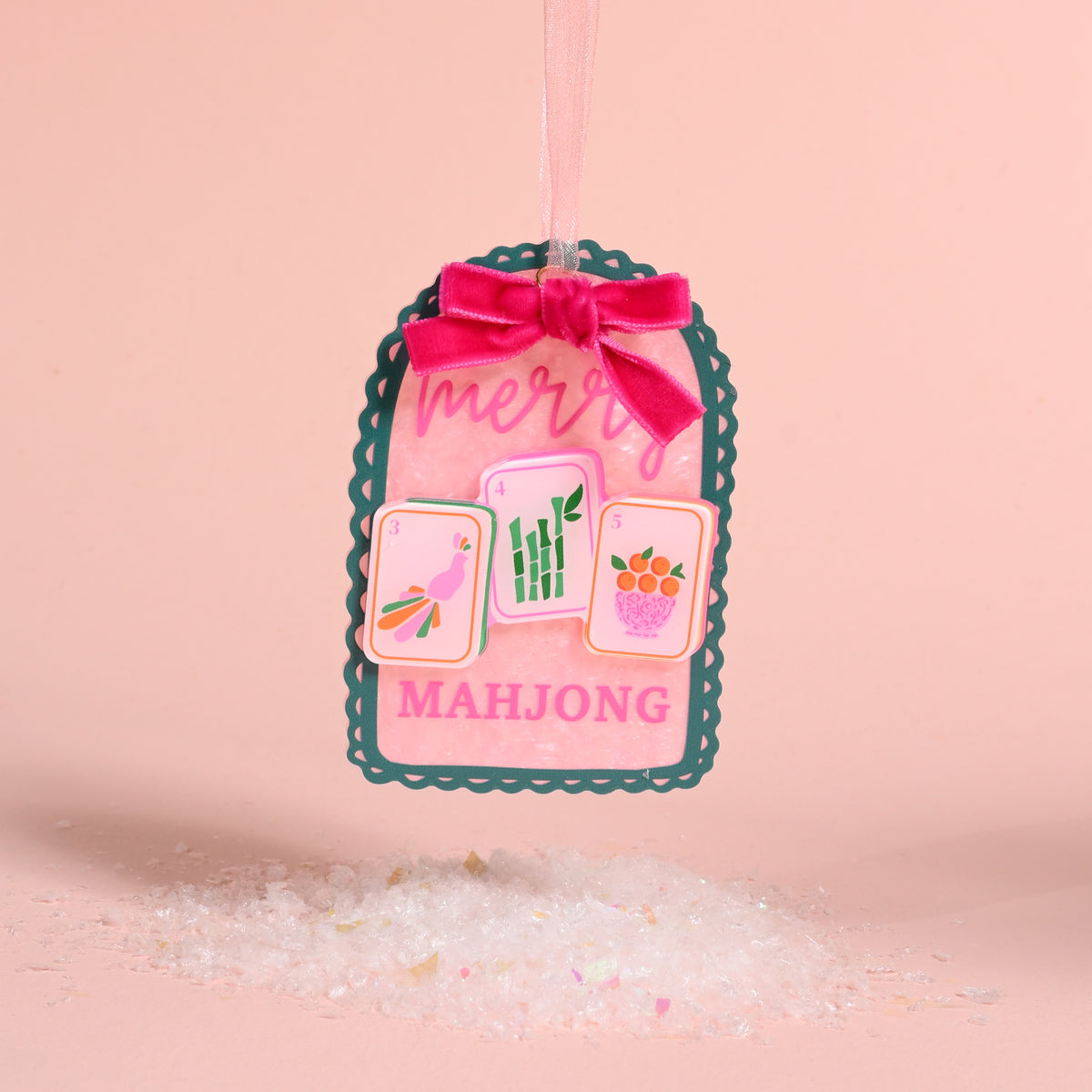 Merry Mahjong Acrylic Ornament in scalloped pink acrylic with a dark green border, featuring three mahjong tiles, merry MAHJONG text, and a pink velvet bow with a ribbon hanger.