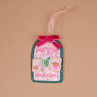 Merry Mahjong Acrylic Ornament shaped like a scalloped tag, featuring the word merry above three mahjong tiles and MAHJONG text, finished with a pink velvet bow.