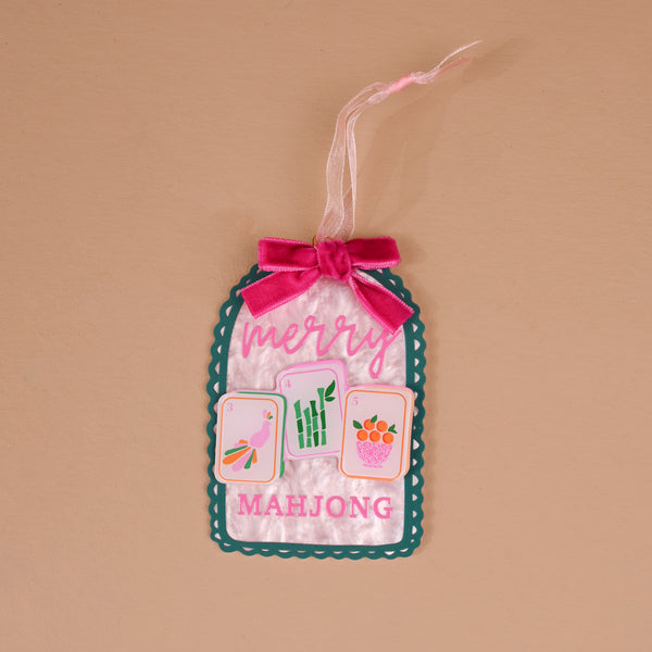 Merry Mahjong Acrylic Ornament shaped like a scalloped tag, featuring the word merry above three mahjong tiles and MAHJONG text, finished with a pink velvet bow.