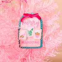 Merry Mahjong Acrylic Ornament shaped like a tag, hanging on a pink tree with text reading merry MAHJONG and illustrations of three mahjong tiles.