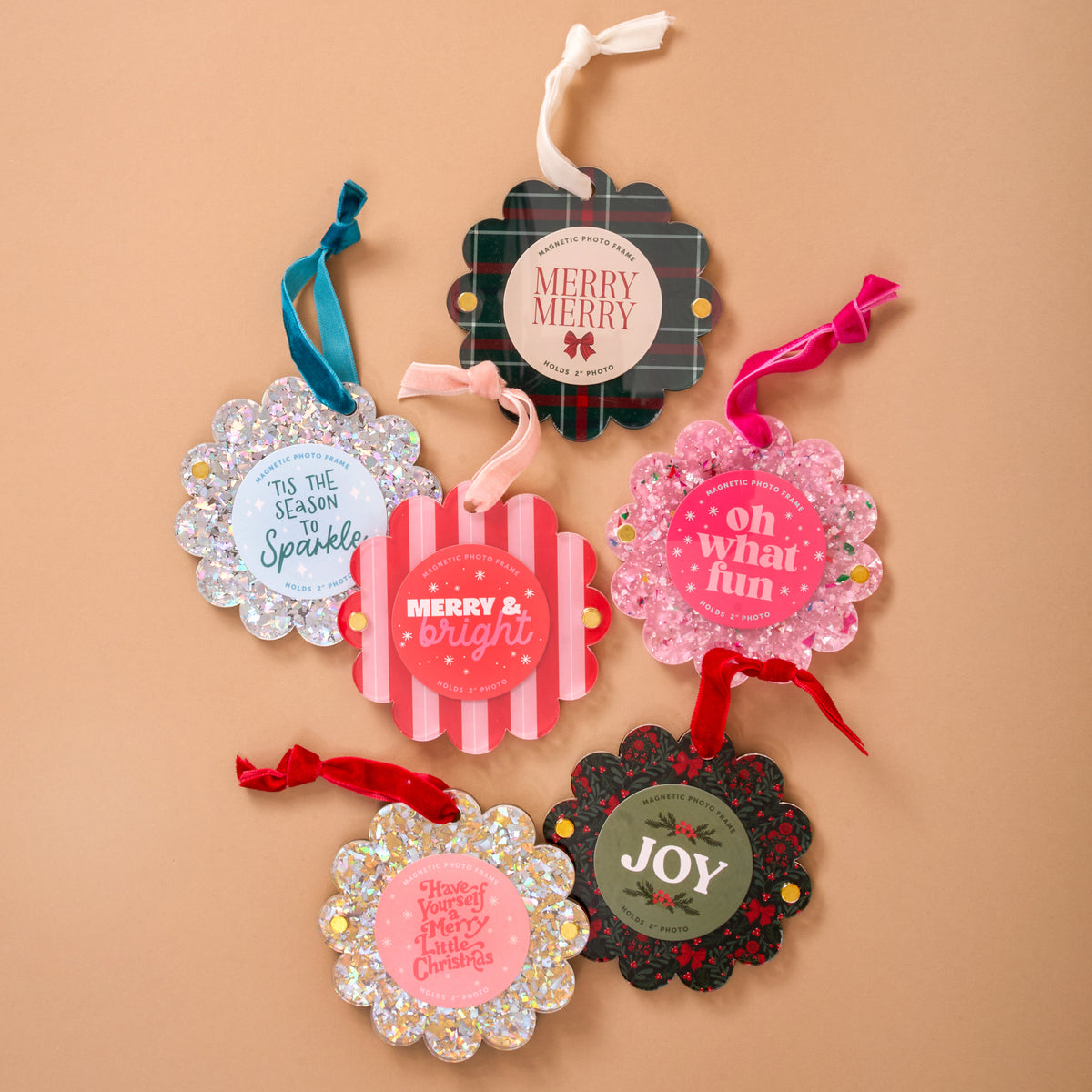 Six holiday gift tags with festive colors, glitter, and messages like "Merry & Bright" are arranged on a tan background—perfect accents for gifts or pairing with The Darling Effect's Confetti Pink Scalloped Round Picture Frame Ornament.