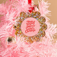 A Gold Glitter Scalloped Round Picture Frame Ornament by The Darling Effect hangs on a light pink Christmas tree, featuring a floral design and the words "Have Yourself a Merry Little Christmas" in red and white. A gold bauble is also visible.