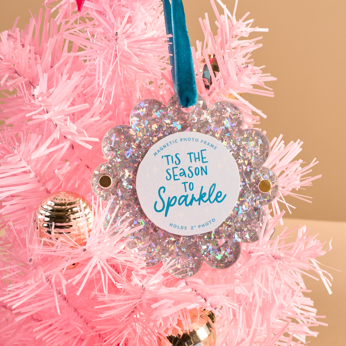 The Darling Effect Silver Glitter Scalloped Round Picture Frame Ornament, reading Tis the season to sparkle with a blue velvet ribbon hanger, hanging on a pink artificial Christmas tree.