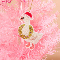 A Merry Silly Goose Handcrafted Beaded Ornament featuring a goose wearing a red Santa hat and a wreath around its neck, hanging on a pink Christmas tree.