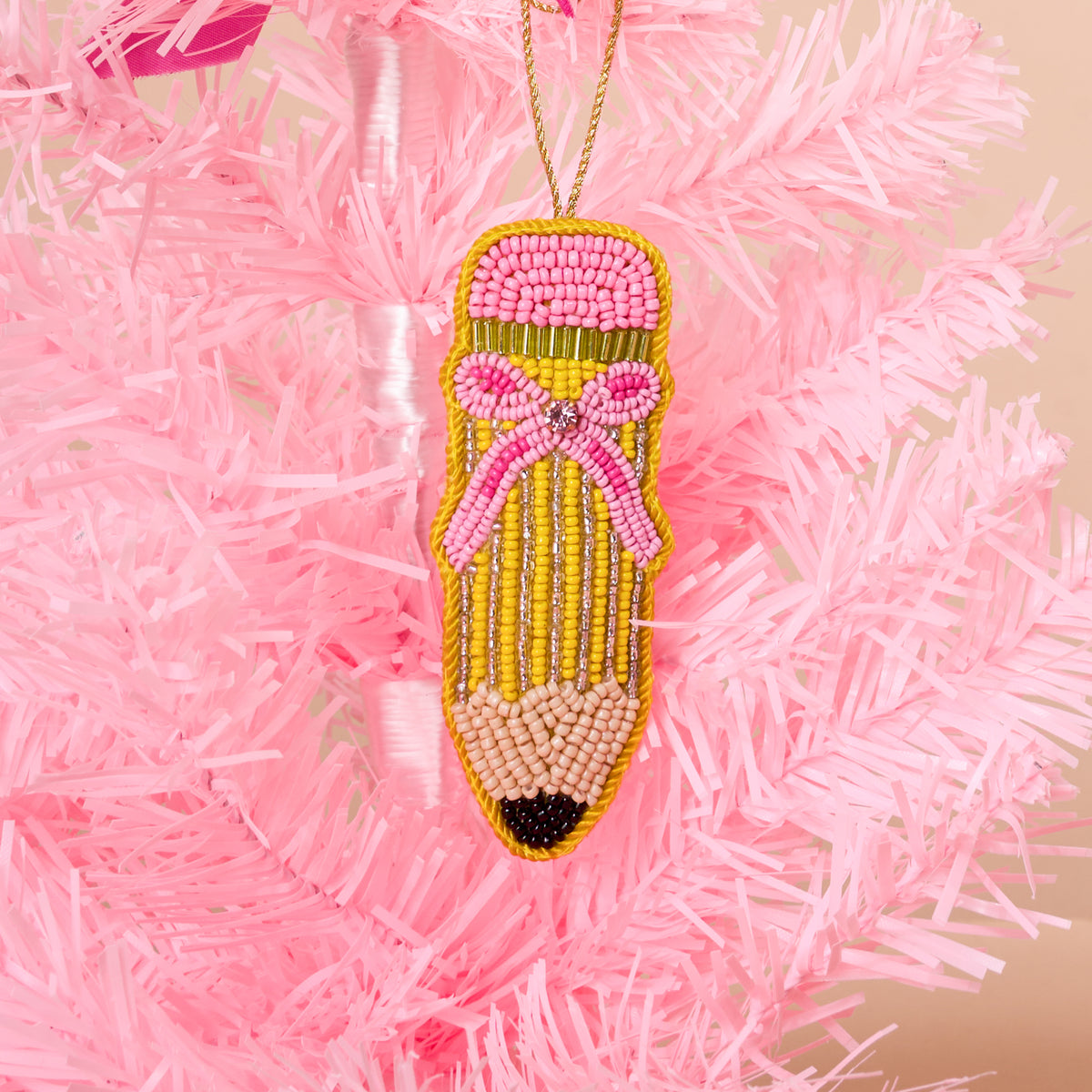 The Darling Effect Pencil Handcrafted Beaded Ornament decorated with pink, yellow, and metallic beads, featuring a pink bow and hanging from a gold string on a pink tree.