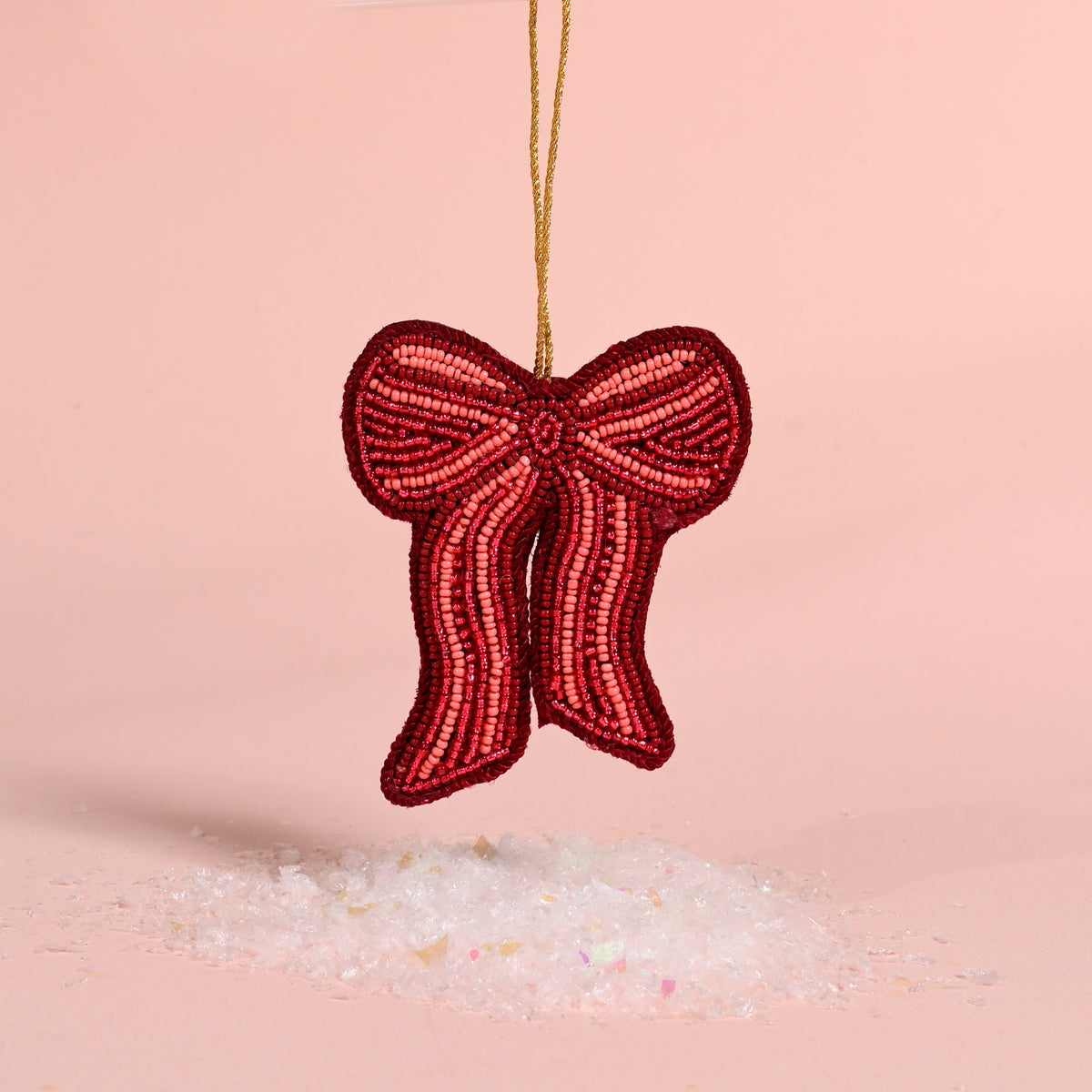 The Darling Effect Red Bow Handcrafted Beaded Ornament hanging above a pile of faux snow.