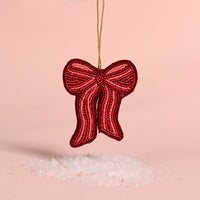 The Darling Effect Red Bow Handcrafted Beaded Ornament hanging above a pile of faux snow.