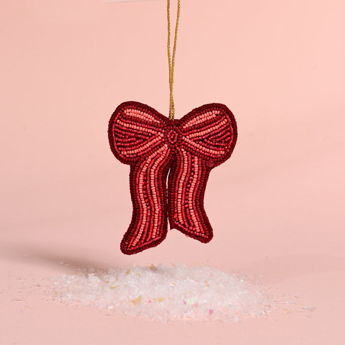 The Darling Effect Red Bow Handcrafted Beaded Ornament hanging above a pile of faux snow.