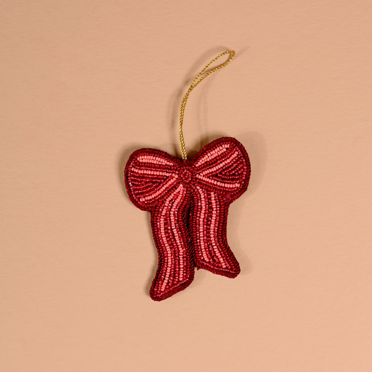 The Darling Effect Red Bow Handcrafted Beaded Ornament is a red bow-shaped decoration made of small glass beads with a gold hanging loop.