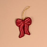 The Darling Effect Red Bow Handcrafted Beaded Ornament is a red bow-shaped decoration made of small glass beads with a gold hanging loop.