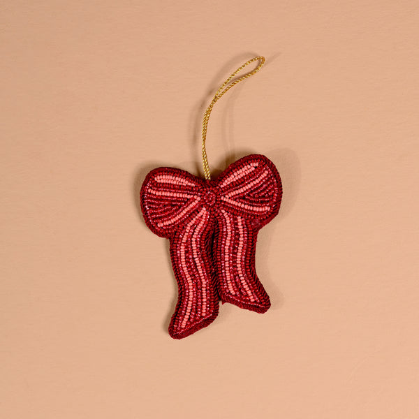 The Darling Effect Red Bow Handcrafted Beaded Ornament is a red bow-shaped decoration made of small glass beads with a gold hanging loop.