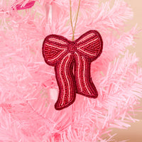 A Red Bow Handcrafted Beaded Ornament from The Darling Effect hangs on a pink artificial tree, adding a festive touch to the holiday décor.