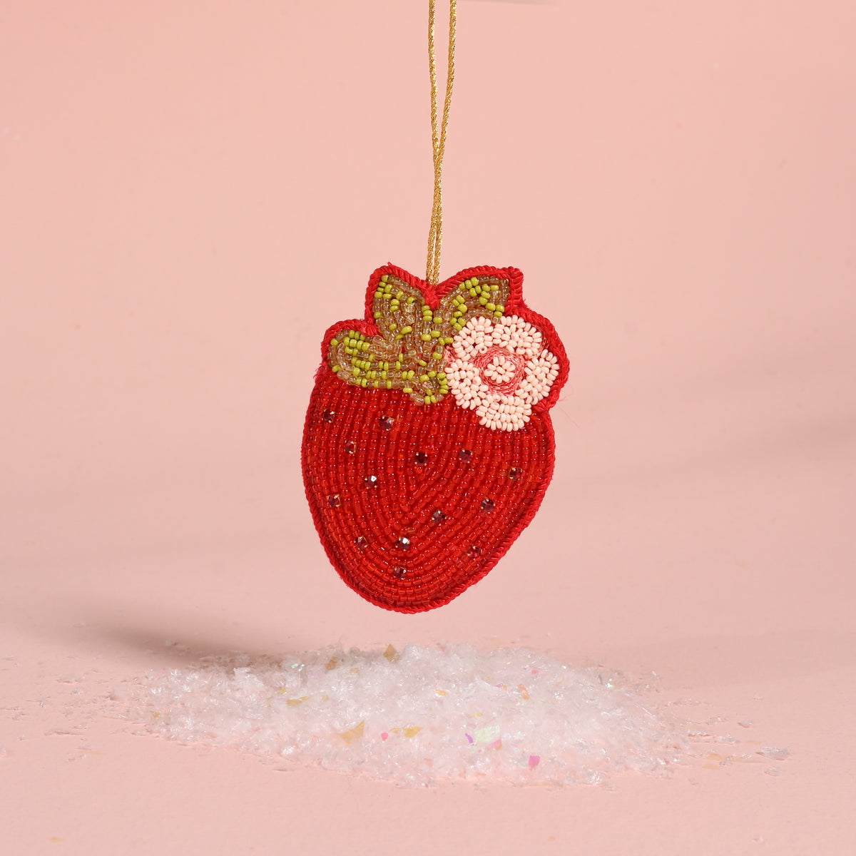 Strawberry Handcrafted Beaded Ornament featuring a green leaf and white flower detail, hanging above a small pile of artificial snow.