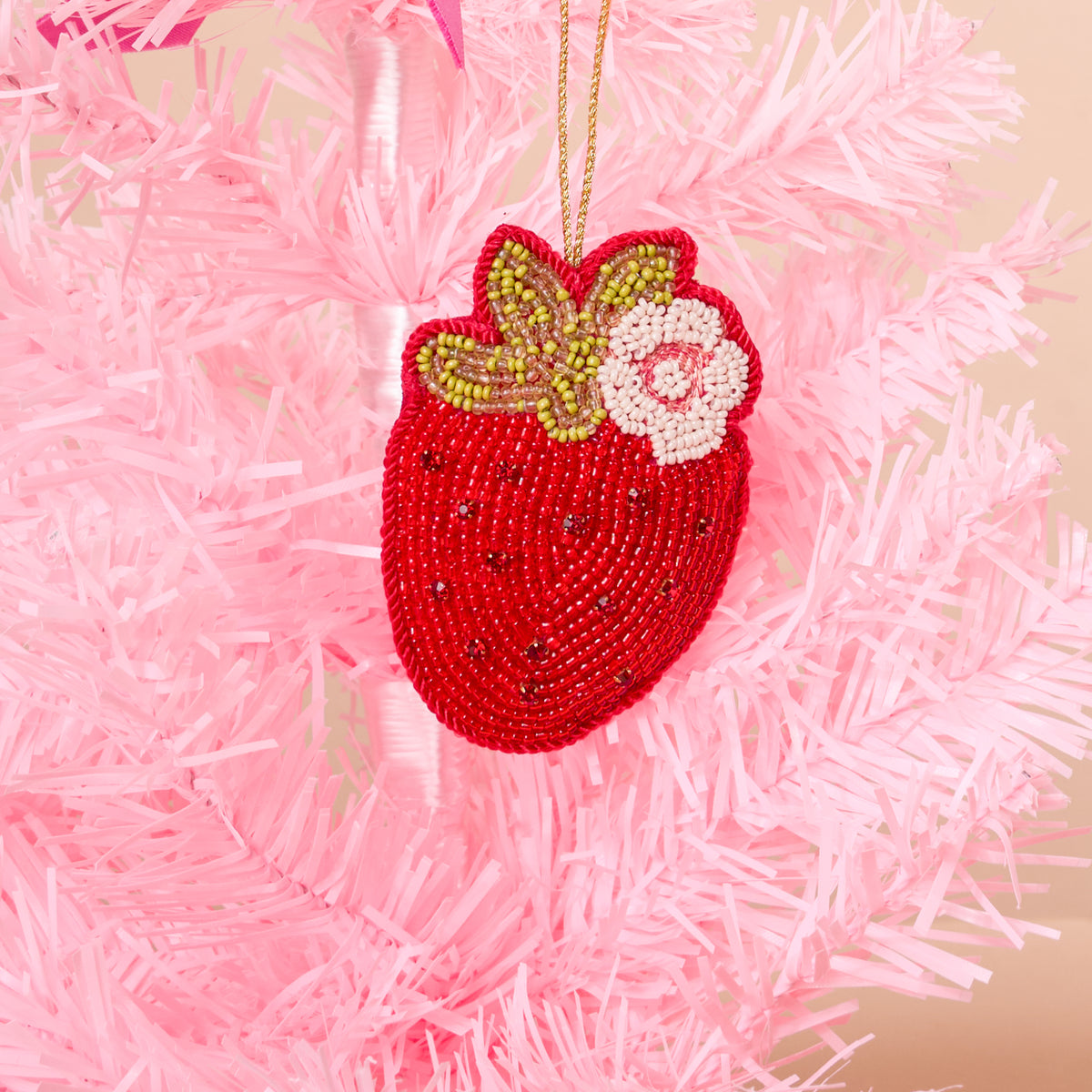 A Strawberry Handcrafted Beaded Ornament featuring a green and white flower accent, hanging on a pink Christmas tree.