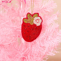 A Strawberry Handcrafted Beaded Ornament featuring a green and white flower accent, hanging on a pink Christmas tree.