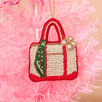 The Darling Effect Tote of the Year Handcrafted Beaded Ornament shaped like a tote bag with red and cream detailing, a green ribbon accent, and a bow charm, hanging on a pink Christmas tree.