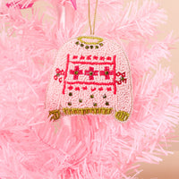 A Christmas Sweater Handcrafted Beaded Ornament shaped like a pink sweater with a geometric pattern, hanging on a pink artificial Christmas tree.
