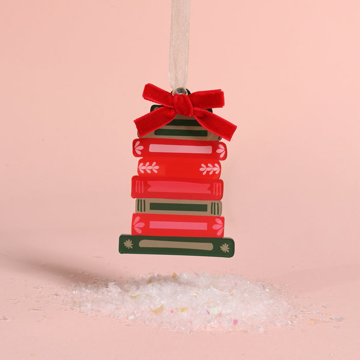 A Bookstack Acrylic Ornament shaped like a stack of red and green books, topped with a red velvet bow for festive holiday styling.