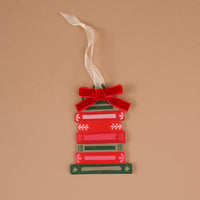 A Bookstack Acrylic Ornament by The Darling Effect featuring a stack of red and green books accented with a red velvet bow and a white ribbon hanger.