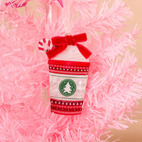 Peppermint Latte Acrylic Ornament shaped like a coffee cup, decorated with a red ribbon bow, a peppermint candy, and a green tree logo, hanging on a pink Christmas tree.