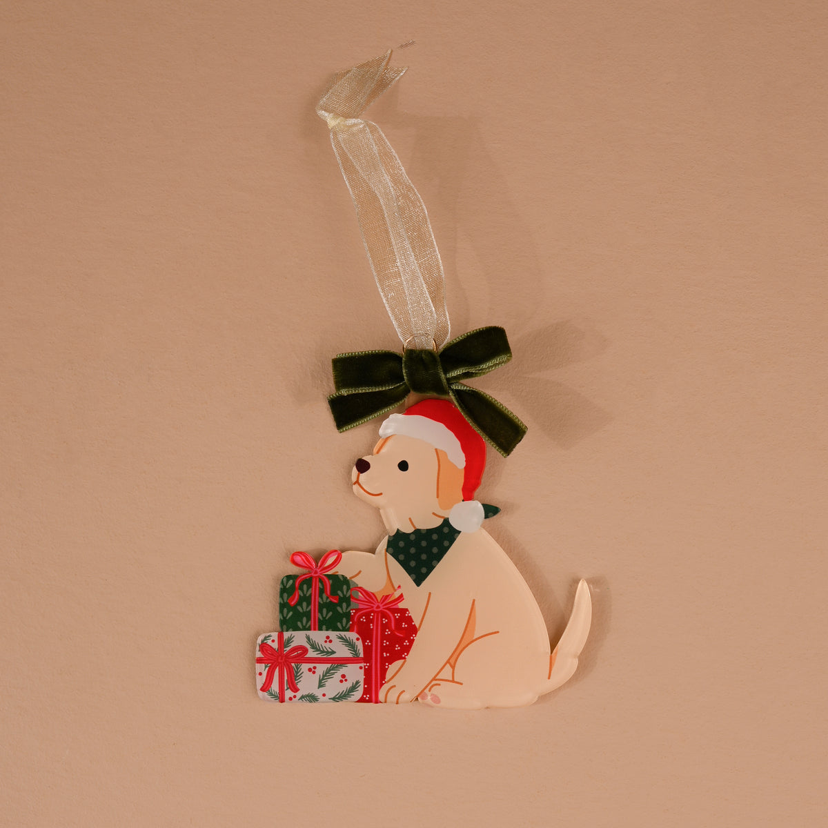 Santa Paws Acrylic Ornament featuring a light-colored puppy in a Santa hat and green bandana, sitting by two wrapped gifts and topped with a dark green velvet bow.