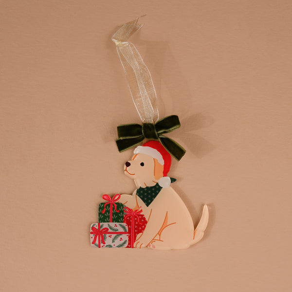 Santa Paws Acrylic Ornament featuring a light-colored puppy in a Santa hat and green bandana, sitting by two wrapped gifts and topped with a dark green velvet bow.