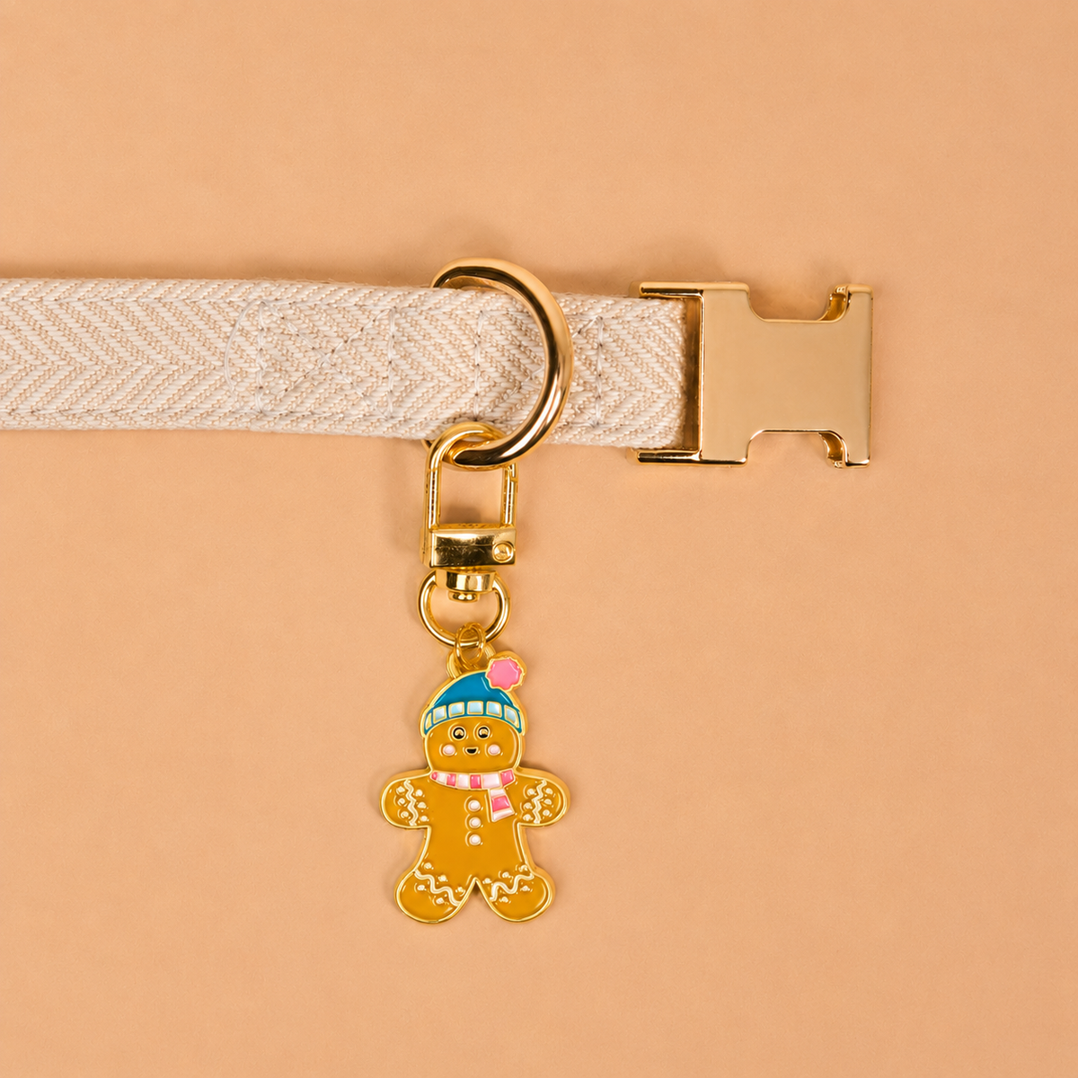The Gingerbread Pawfect Collar Charm features a gold-toned gingerbread man with a blue hat and striped scarf, attached to a cream-colored pet collar accessory.