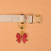 A gold-tone metal Holiday Bow Pawfect Collar Charm hanging from a pet accessory collar.