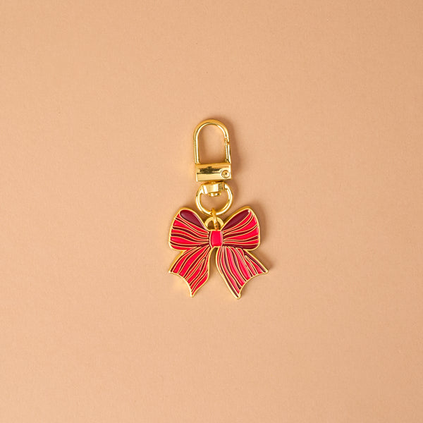 The Holiday Bow Pawfect Collar Charm by The Darling Effect is a gold-toned metal pet accessory in the shape of a red bow, featuring a lobster clasp for easy attachment to collar charms.
