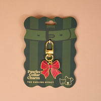 Holiday Bow Pawfect Collar Charm, a red and gold bow-shaped charm with a gold lobster clasp, attached to green striped display packaging for dog and cat collars.