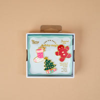 Holiday Magic The Pin Pack features three holiday-themed enamel pins: a pink stocking, a decorated Christmas tree, and a gingerbread man.