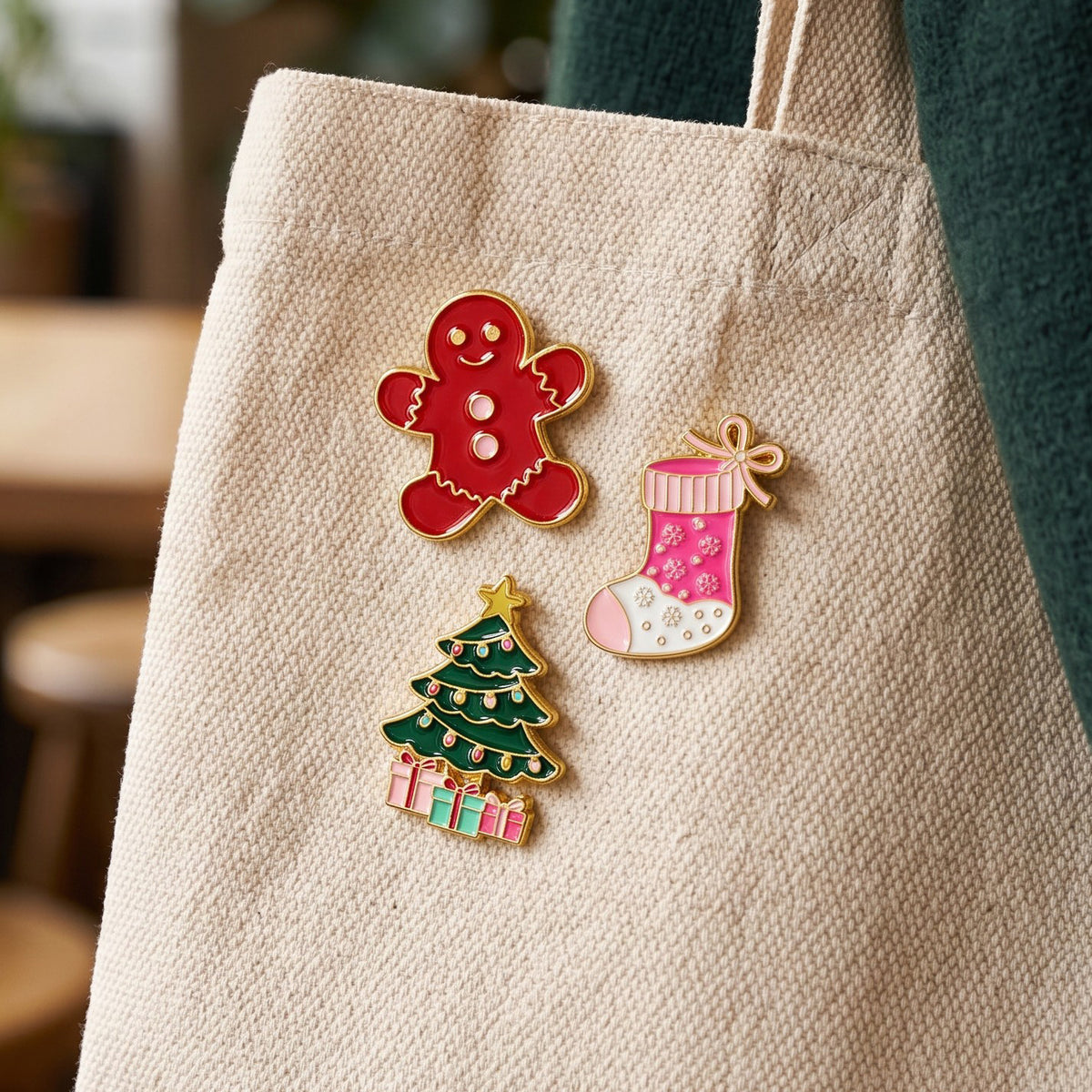 Holiday Magic The Pin Pack features three holiday-themed enamel pins—a gingerbread man, a Christmas tree, and a stocking—pinned to a beige canvas tote bag as collectible accessories.