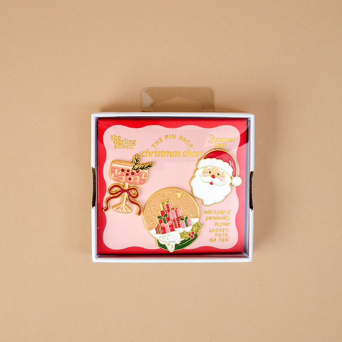 Christmas Cheer The Pin Pack features three collectible pins in a box: a pink champagne glass, a snow globe with presents, and a Santa Claus head.