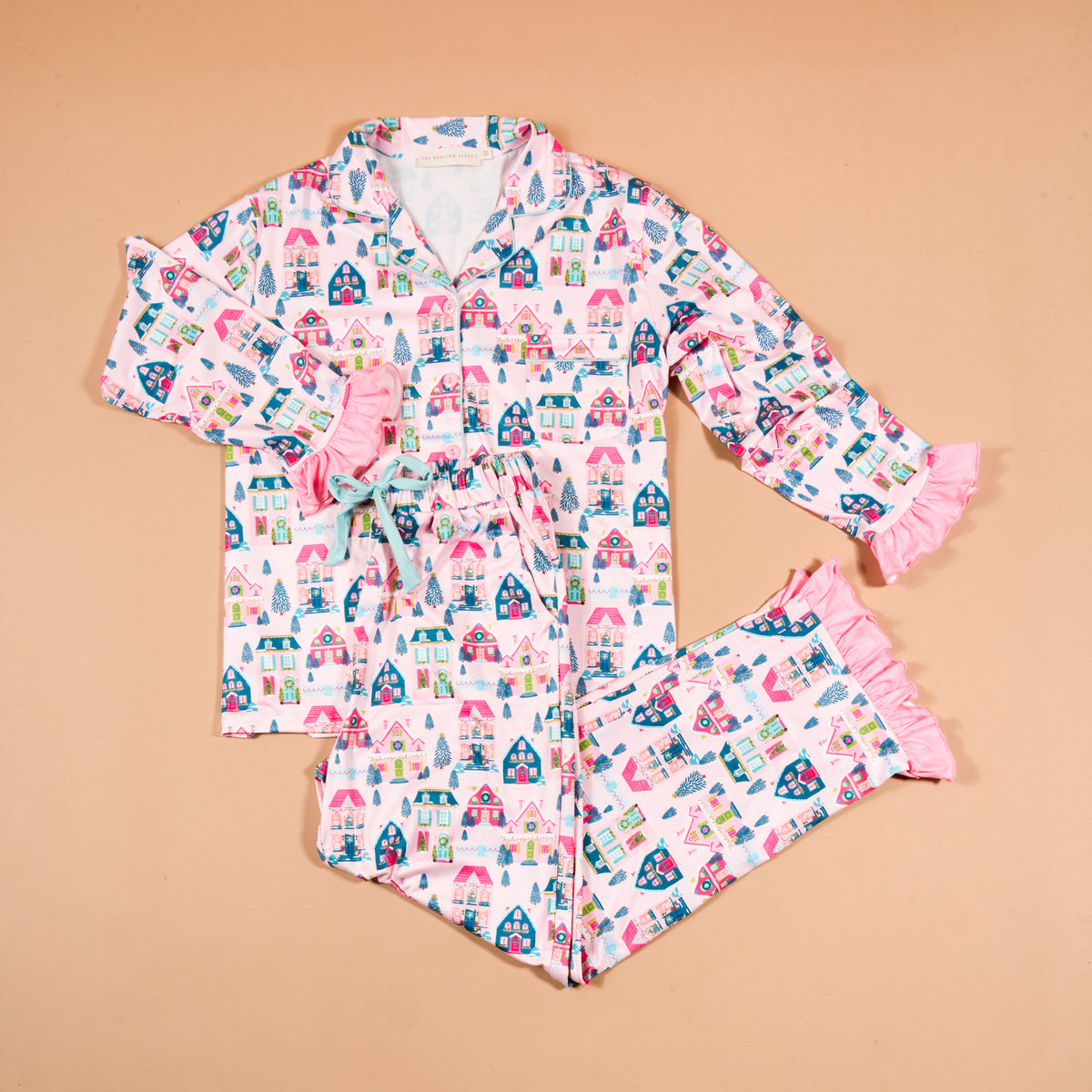 Sugarplum Lane Sweet Dreams Pajama Pants Set featuring a long-sleeved button-up shirt and matching pants with a pink Christmas village print and pink ruffled trim.
