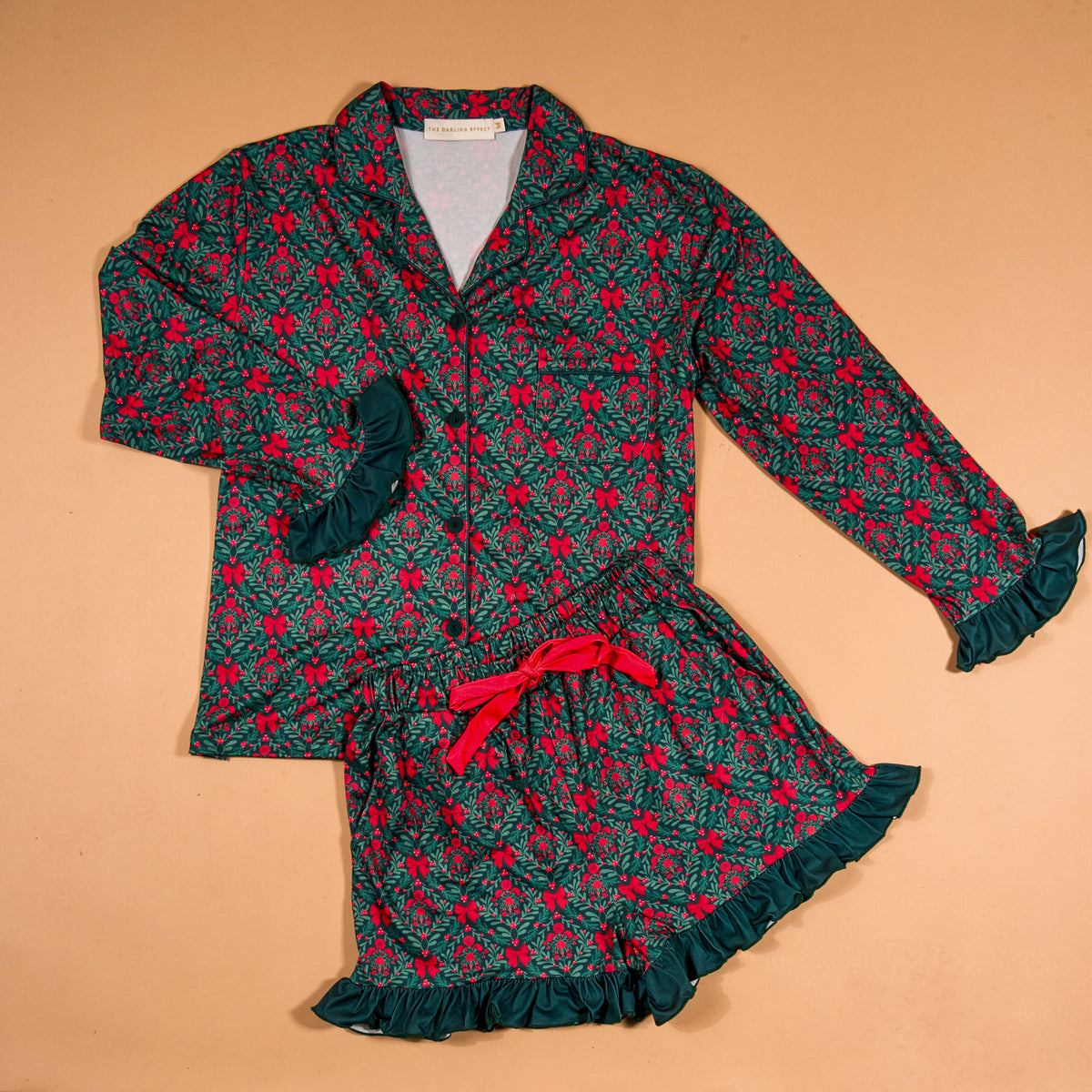 A Merry Moment Sweet Dreams Pajama Shorts Set featuring a long-sleeved button-up top and matching shorts with a green and red holly print, finished with dark green ruffled cuffs and hems.