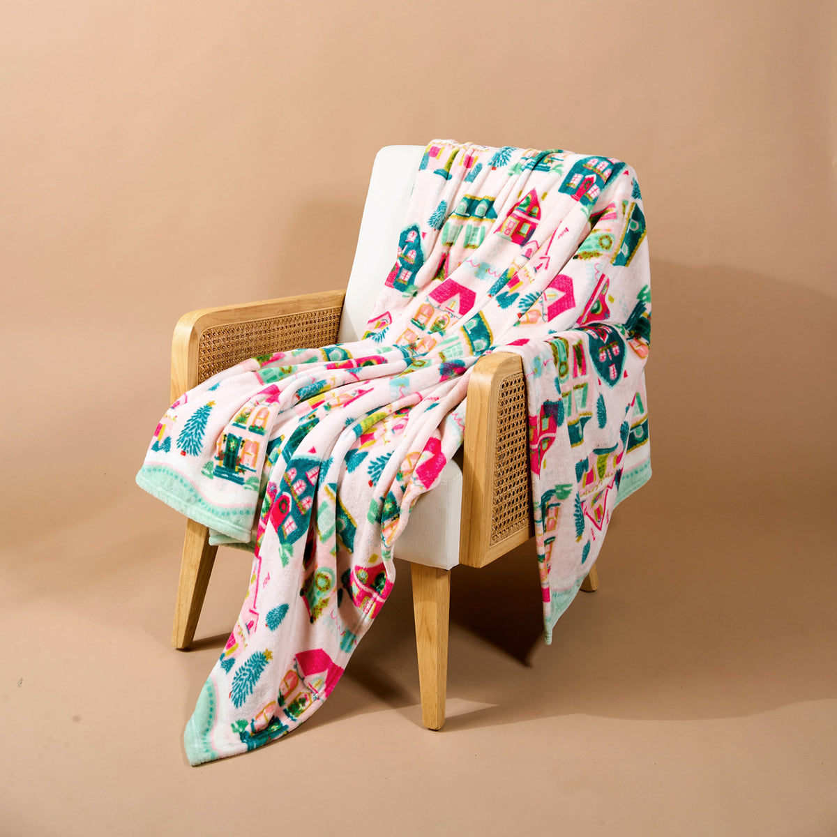 A Sugarplum Lane Snuggle Up Plush Blanket with colorful houses and trees draped over a wooden armchair.