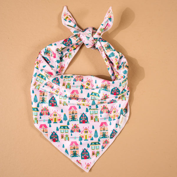 Sugarplum Lane Bow-Wow Pet Bandana featuring a satin repeating pattern of colorful holiday cottages and pine trees on a light pink background.